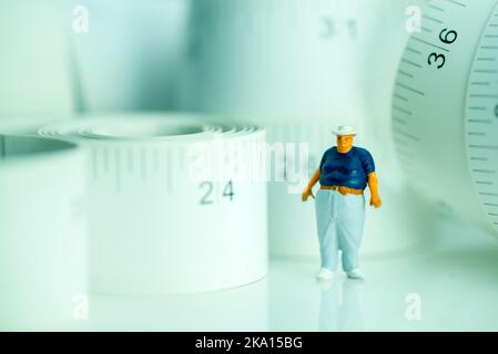 Miniaturfigur eines übergewichtigen Mannes gegen Maßband. Stockfoto