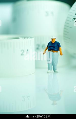 Miniaturfigur eines übergewichtigen Mannes gegen Maßband. Stockfoto