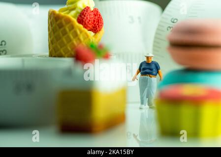 Miniaturfigur eines übergewichtigen Mannes gegen Maßband und ungesunde Lebensmittel. Stockfoto