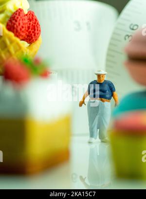 Miniaturfigur eines übergewichtigen Mannes gegen Maßband und ungesunde Lebensmittel. Stockfoto