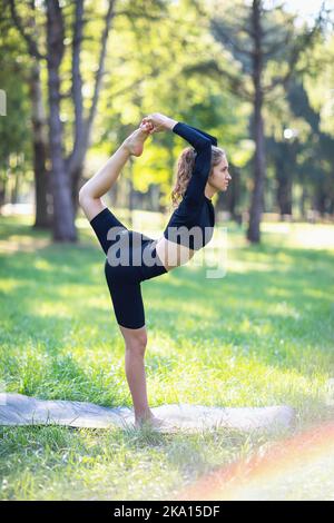 Frau in Sport schwarzen Kleidern üben Yoga tun Natarajasana Übung, Pose des Königs der Tänzer, die Ausübung an einem warmen Sommermorgen stehen o Stockfoto