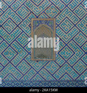 Blaue und türkisfarbene Mosaikdekor und Gitterfenster an der Außenwand von Sher Dor madrassa am historischen Registan-Platz in Samarkand, Usbekistan Stockfoto