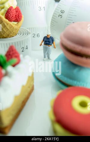 Miniaturfigur eines übergewichtigen Mannes gegen Maßband und ungesunde Lebensmittel. Stockfoto