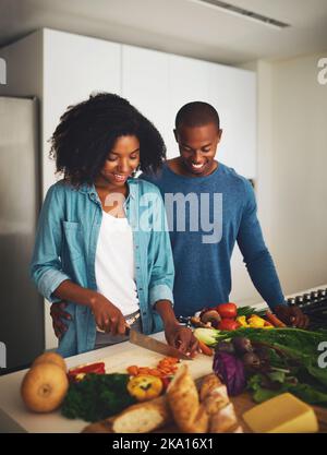 Mein Mann hilft immer in der Küche. Ein fröhliches junges Paar bereitet tagsüber gemeinsam in der Küche zu Hause Essen zu. Stockfoto