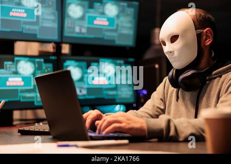 Cyber-Terrorist trägt Maske Hacking Datenbank-Server, Hacker mit Haube brechen in Computersystem und aktivieren Virus, um Malware zu erstellen. Geheimnisvoller Betrüger, der Big Data gestohlen hat. Stockfoto