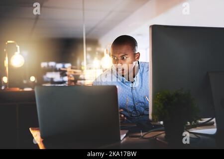 Er weiß, was es braucht, um erfolgreich zu sein. Ein hübscher junger Geschäftsmann, der einen Computer während einer späten Nacht in einem modernen Büro benutzt. Stockfoto