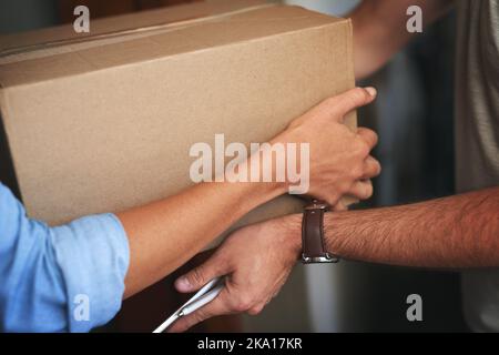 Übergabe einer weiteren erfolgreichen Lieferung. Nahaufnahme eines Kuriers, der eine Lieferung an einen Kunden bei sich zu Hause macht. Stockfoto