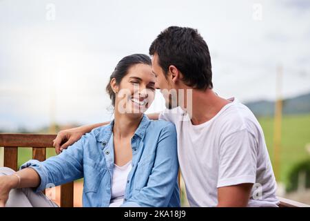 Es ist ein im Himmel gemachtes Streichholz. Ein liebevolles junges Paar, das draußen auf einer Bank sitzt. Stockfoto