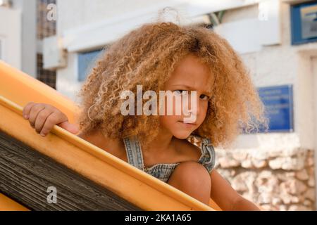 Porträt eines kleinen wütenden Mädchens auf dem Hintergrund eines Sommerspielplatzes Stockfoto