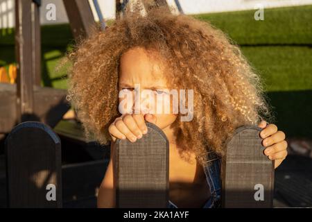 Porträt eines kleinen wütenden Mädchens auf dem Hintergrund eines Sommerspielplatzes Stockfoto