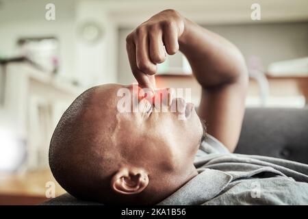 Ich bin nicht in der Stimmung für diesen Tag. Ein gestresster junger Mann liegt auf einer Couch, während er seine Nase in Unannehmlichkeiten drinnen zu Hause während des Tages hält. Stockfoto