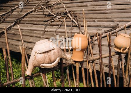 Alte Tontöpfe hängen einfach an einem Weidenzaun. Ukrainische ethnische Gerichte, traditionelle Kultur der Ukraine Stockfoto