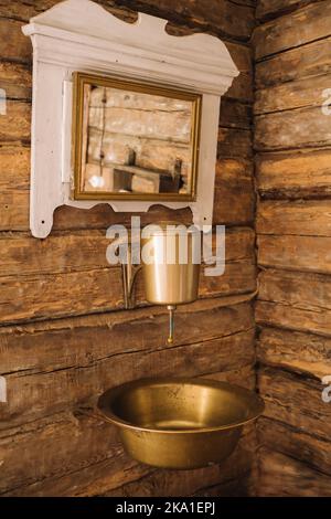 Vintage-Aufnahme eines alten Metallwaschbeckens und Spiegels in einem Holzhaus im Dorf Stockfoto