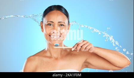 Zahnmedizin, Gesundheit und Frau putzen Zähne mit Zahnbürste, Zahnpasta und Wasser spritzen auf blauem Studiohintergrund. Gesundheitswesen, Selbstpflegeprodukte und oral Stockfoto