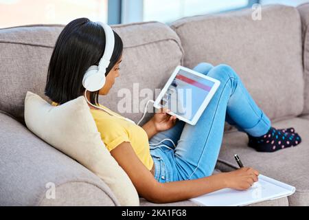 Aufholen mit den neuesten Melodien. Ein Teenager-Mädchen, Musik zu hören und mit einem Tablet zu Hause. Stockfoto