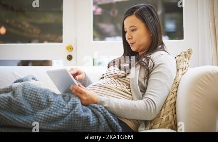 Stöbern Sie durch eine Reihe von Tipps und Tipps für die Schwangerschaft. Eine Schwangerin mit einem digitalen Tablet zu Hause. Stockfoto