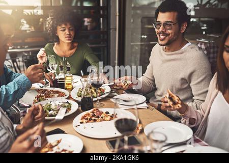 Wir tauchten wirklich in diese Pizza ein. Eine Gruppe fröhlicher junger Freunde, die zusammen Pizza aßen, während sie an einem Tisch im Restaurant saßen. Stockfoto