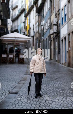 Eine Frau mit einem Regenschirm, die durch eine Innenstadt von Porto, Portugal, schlendert. Stockfoto