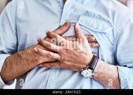 Der Schmerz ist genau hier. Ein unkennbarer Mann hält seine Brust, während er zu Hause mit Sodbrennen leidet. Stockfoto