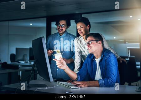 Gemeinsam lösen sie Probleme noch schneller. Eine Gruppe von Programmierern, die nachts an einem Computer im Büro arbeiten. Stockfoto