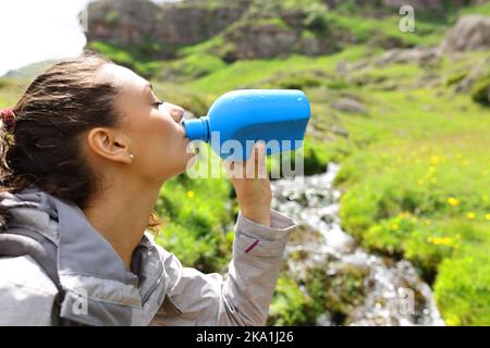 Trekker Trinkwasser aus der Kantine neben einem Bach im Berg Stockfoto