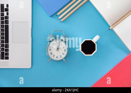 Flach liegend, Wecker und eine Tasse Kaffee am Arbeitsplatz. Stockfoto