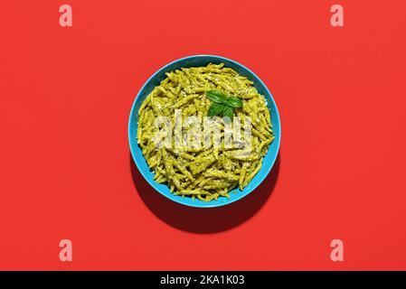 Trofie al Pesto, ein köstliches italienisches Gericht, minimalistisch auf einem roten Tisch. Kurze Teigwaren namens Trofie mit Pesto-Sauce und Parmesan. Stockfoto