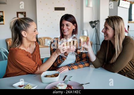 Fröhliche Freundinnen toasten und lächeln beim gemeinsamen Brunch in einem Café. Stockfoto