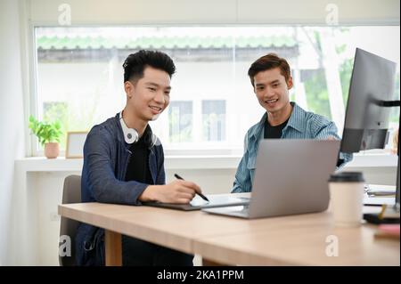 Zwei professionelle junge asiatische Programmierer oder Fotoredakteure arbeiten im Büro zusammen, diskutieren und Brainstorming. Stockfoto