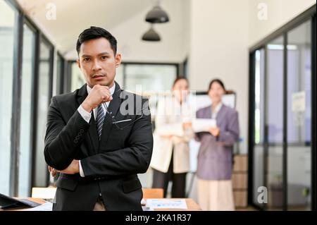In seinem Büro steht ein professioneller und hübscher asiatischer Geschäftsmann oder männlicher Chef im formellen Geschäftsanzug. Stockfoto
