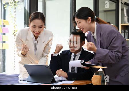 Fröhliche und überfröhliche, tausendjährige asiatische Geschäftsleute feiern den Projekterfolg, den Projektsieg, die Genehmigung des Projekts, den Geschäftsabschluss und den Gewinn eines neuen CO Stockfoto