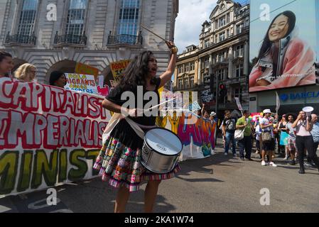 London, Großbritannien. 18. Juni 2018. Eine Frau, die auf eine Trommel schlägt, führt einen Anti-Kapitalismus-marsch an den riesigen elektronischen Bildschirmen am Piccadilly Circus vorbei. Stockfoto