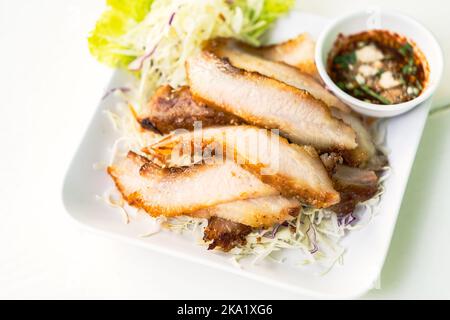 Gegrillter Schweinefleisch-Hals, Nahaufnahme beliebter thailändischer Speisen Snack gegrillter Schweinefleisch-Hals auf weißem Teller, Bettwäsche mit frischem Gemüse und würziger Sauce, ausgewählt für Stockfoto