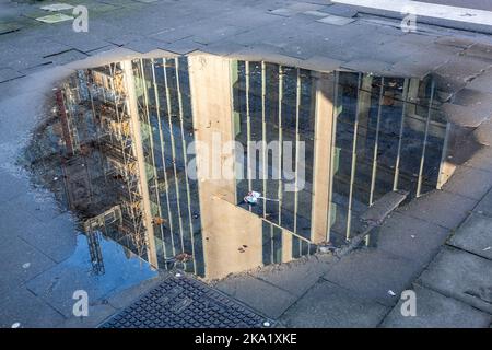 Spiegelbild eines im Bau befindlichen Gebäudes in einer Pfütze auf einem Bürgersteig in Brüssel, im Viertel Gare du Nord. Stockfoto