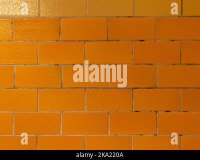 Nahaufnahme einer gelb gefliesten Wand. Hintergrundstruktur einer alten Fassade im Inneren eines Gebäudes. Glänzendes Materialdesign mit schmutzigen Fliesenfugen. Stockfoto