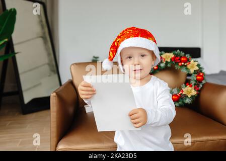 Ein Kind schreibt einen Brief an den Weihnachtsmann. Die Hände des Kindes, ein Blatt Papier, hält Malish den Brief. Das Konzept von Neujahr und Weihnachten Stockfoto