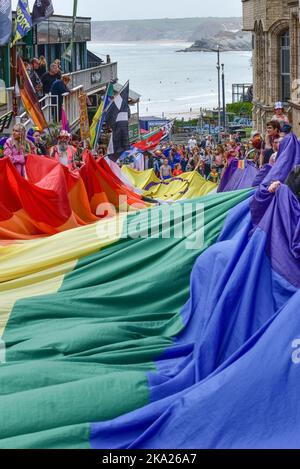 Das farbenfrohe Cornwall ist stolz auf das Banner der Pride-Flagge, das von den Teilnehmern der Parade im Zentrum von Newquay in Großbritannien gehalten wird. Stockfoto