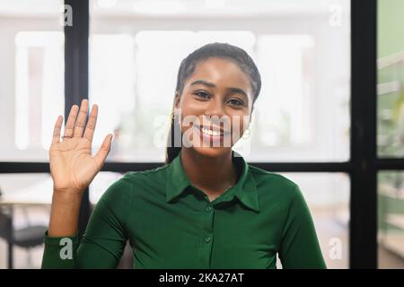 Freundliche, entzückende afroamerikanische Büroarbeiterin Geschäftsfrau, Freiberuflerin mit Afro-Frisur, fröhlich winkend, lächelnd und hallo sprechend, Hello-Zeichen machend, einen Neuling begrüßend und begrüßend Stockfoto