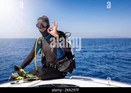 Ein Taucher sitzt auf einem Boot und signalisiert das OK-Zeichen Stockfoto