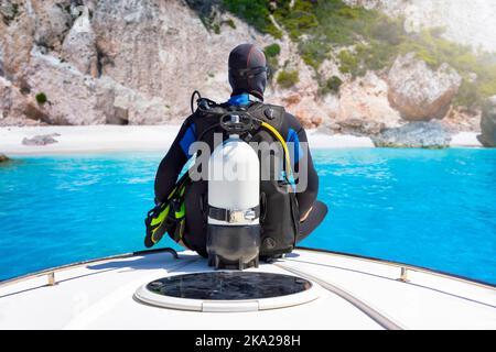 Ein Taucher mit seiner Ausrüstung sitzt auf einem Bug eines Bootes Stockfoto