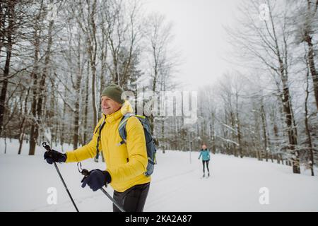 Älterer Mann, der vor einem verschneiten Wald Skilanglauf macht. Stockfoto