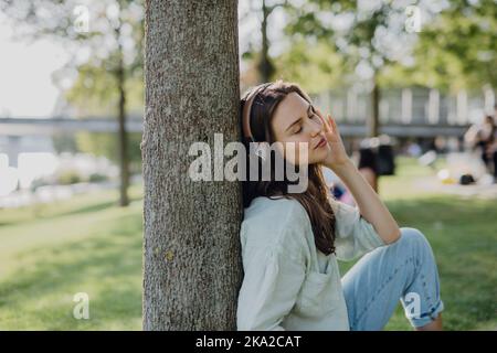 Porträt einer jungen Frau, die im Stadtpark über Kopfhörer Musik hört. Stockfoto