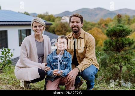 Glückliche Familie hält Kunststoff-Modell der Windenergieanlage. Alternative Energie, Ressourcenschonung und nachhaltiges Lifestyle-Konzept. Stockfoto