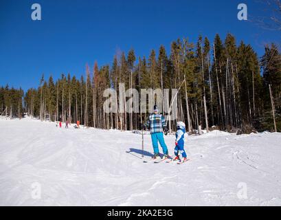 Der glückliche kleine Junge lernt während der Winterferien in verschneiten Bergen an einem sonnigen, kalten Tag mit seinem Vater Ski zu fahren. Ein interessanter Aktivurlaub mit dem f Stockfoto