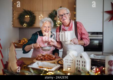 Glückliche Senioren backen gemeinsam Weihnachtskuchen in ihrer Küche. Stockfoto