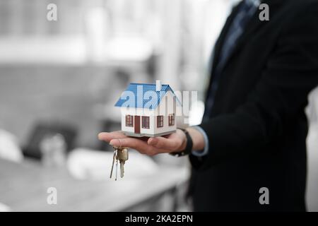 Buchhalter, Geschäftsmann, Immobilienmakler, asiatischer Geschäftsmann, der Modellhaus und Schlüssel an Kunden zusammen mit der Berechnung des Hausinteresses überreicht Stockfoto