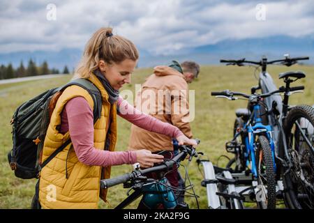 Junge Familie bereitet sich auf eine Fahrradtour in der Natur vor, indem sie Fahrräder von den Autoablagen ablegt. Gesundes Lifestyle-Konzept. Stockfoto