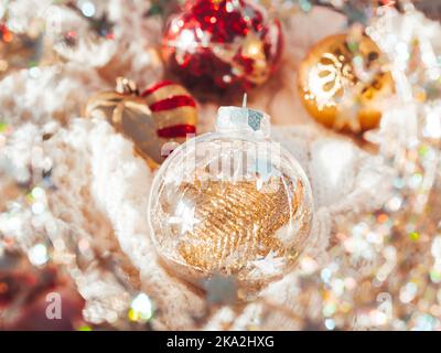 Dekorative Kugeln für Weihnachtsbaum auf Zopfmuster-Pullover. Transparente Kugel mit roten, goldenen Winkeln im Inneren. Winterurlaub. Neues Jahr Stockfoto