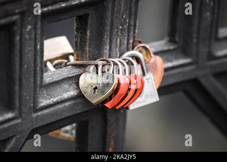 Liebesschlösser an der Brücke befestigt. Rotes Love Heart Messing-Vorhängeschloss, das über Brückenschienen an Metall befestigt ist. Stockfoto