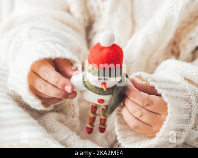 Kind mit Filz dekorativen Schneemann für Weihnachtsbaum. Boy in Zopfmuster-Oversize-Pullover. Gemütliches Outfit für kuscheliges Wetter. Charakter mit Weihnachtsmütze. Stockfoto